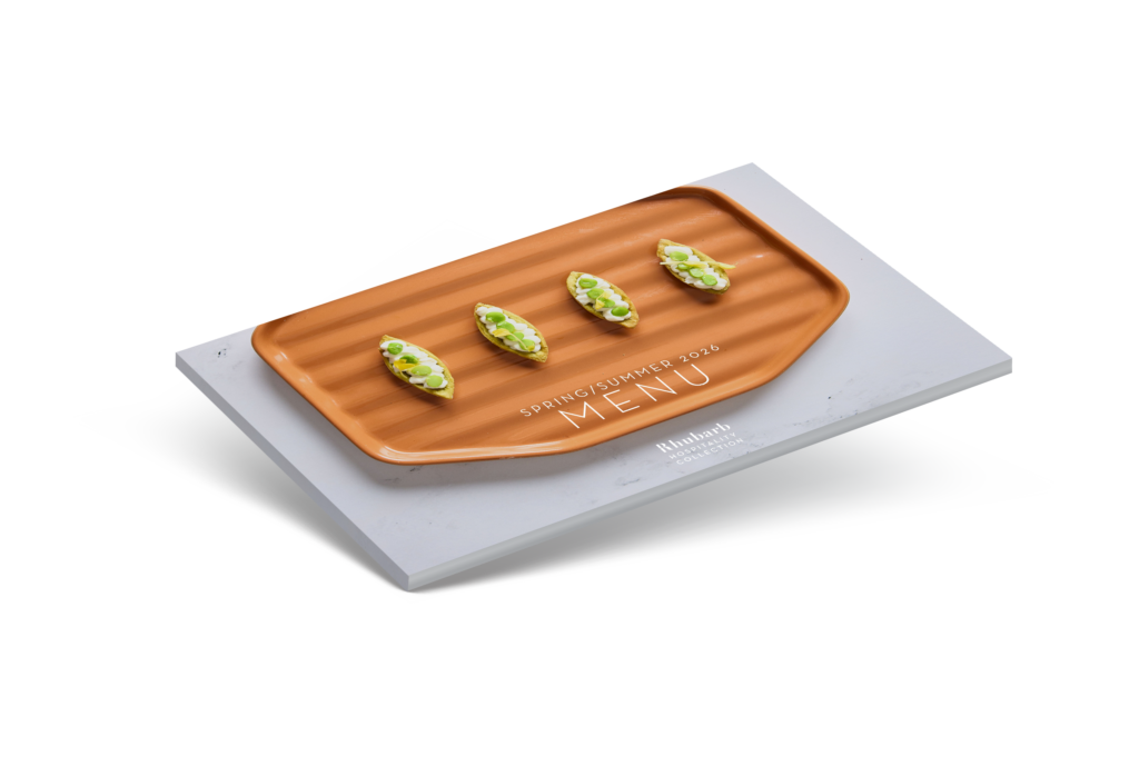 A rectangular orange platter with four small appetizers, garnished with green herbs, is placed on top of a gray menu card that reads "SPRING/SUMMER 2023 MENU." The background is white.